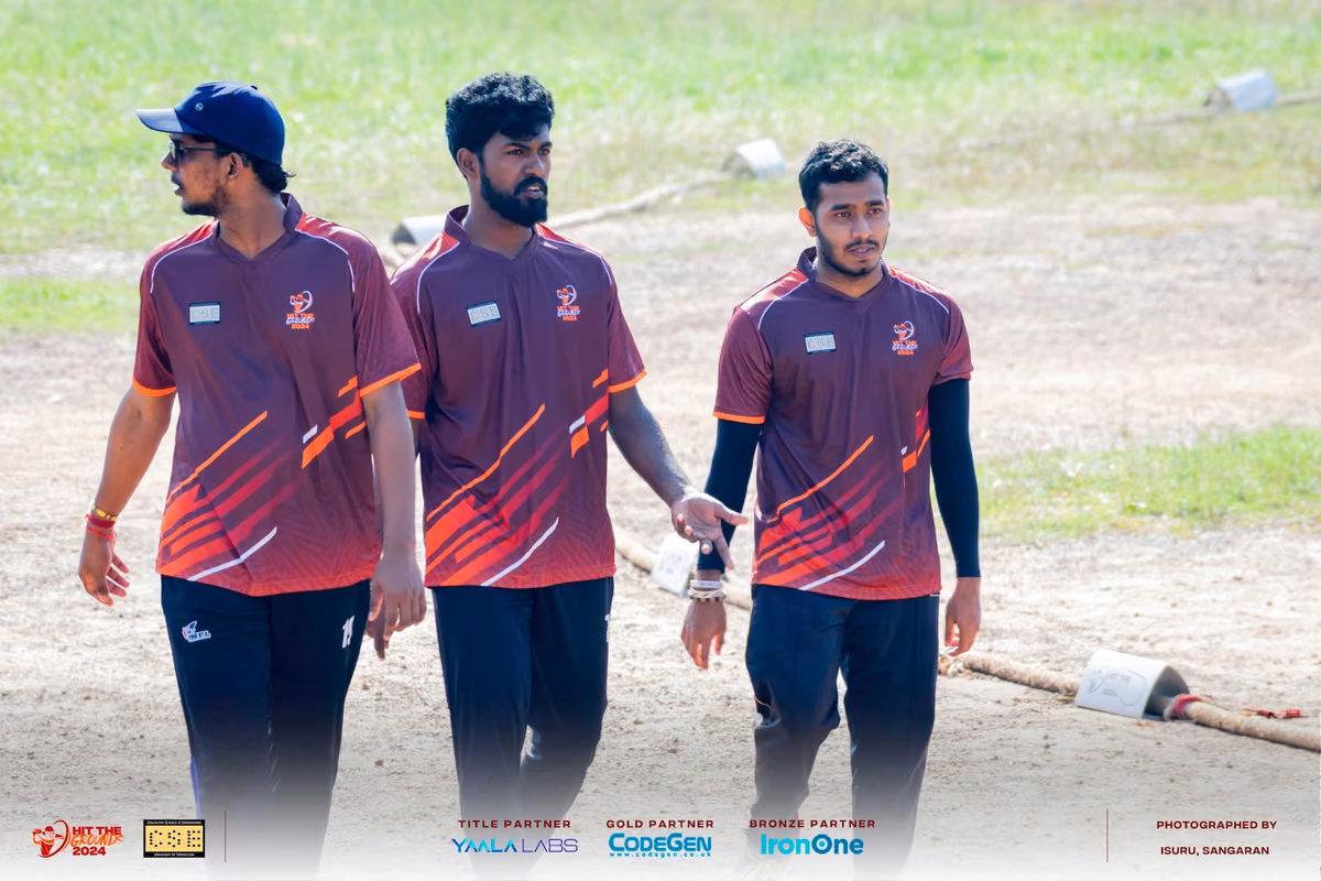 Three players in maroon and orange jerseys walking across the grass