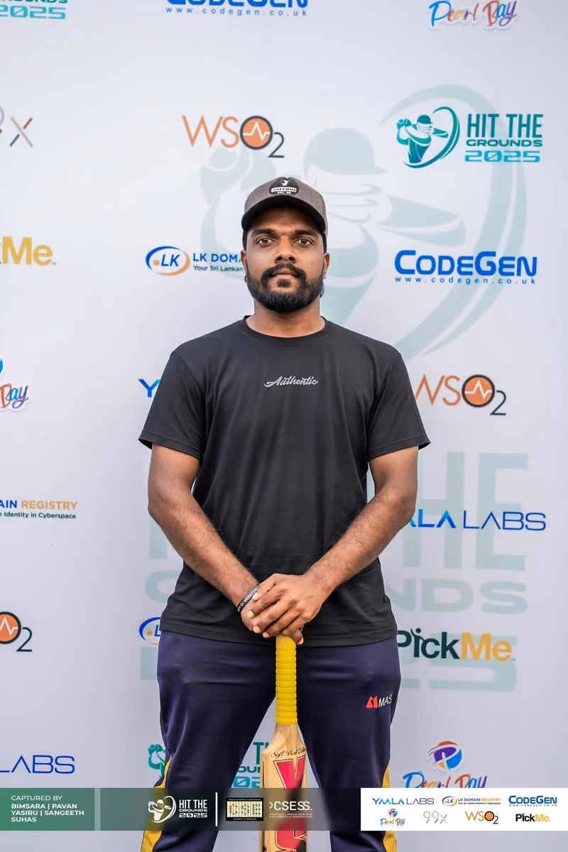 A man in a black shirt holding a bat in front of the sponsor backdrop