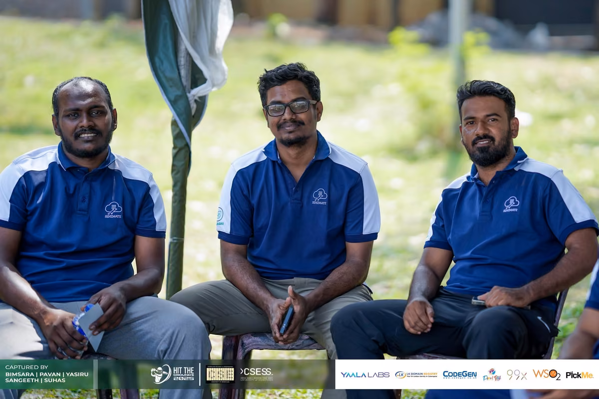 Three men in blue polos seated in the shade