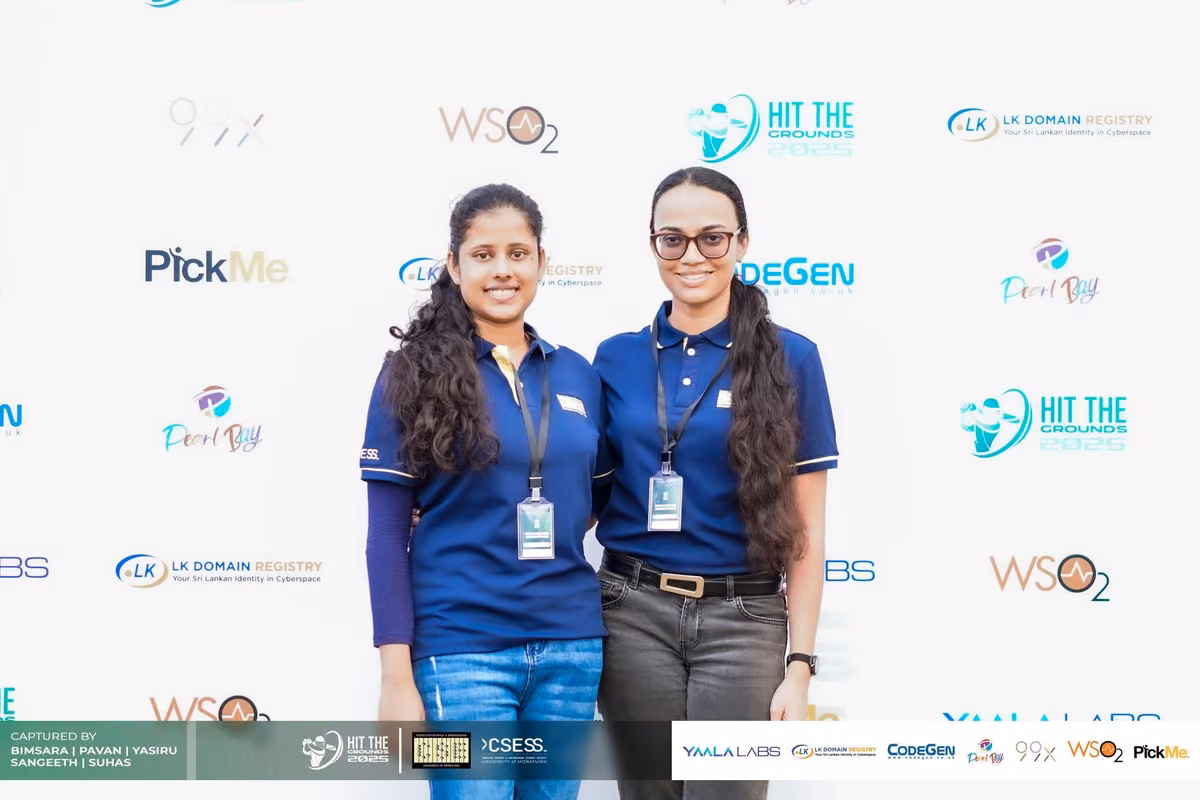 Two women in blue shirts smiling in front of the sponsor backdrop